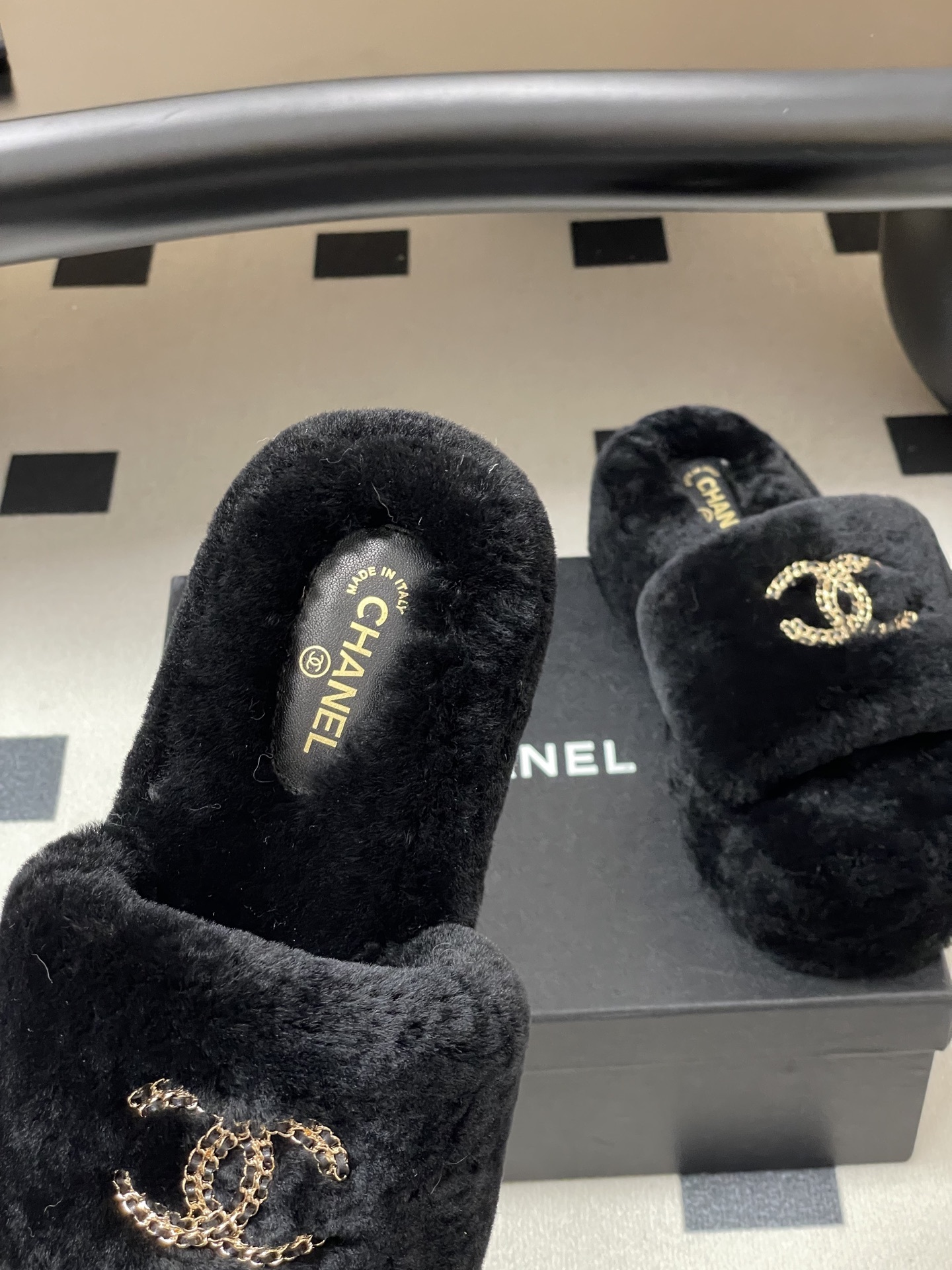 Pair of black Chanel shearling platform slides with gold chain interlocking CC logo on a black table. - Hình 7