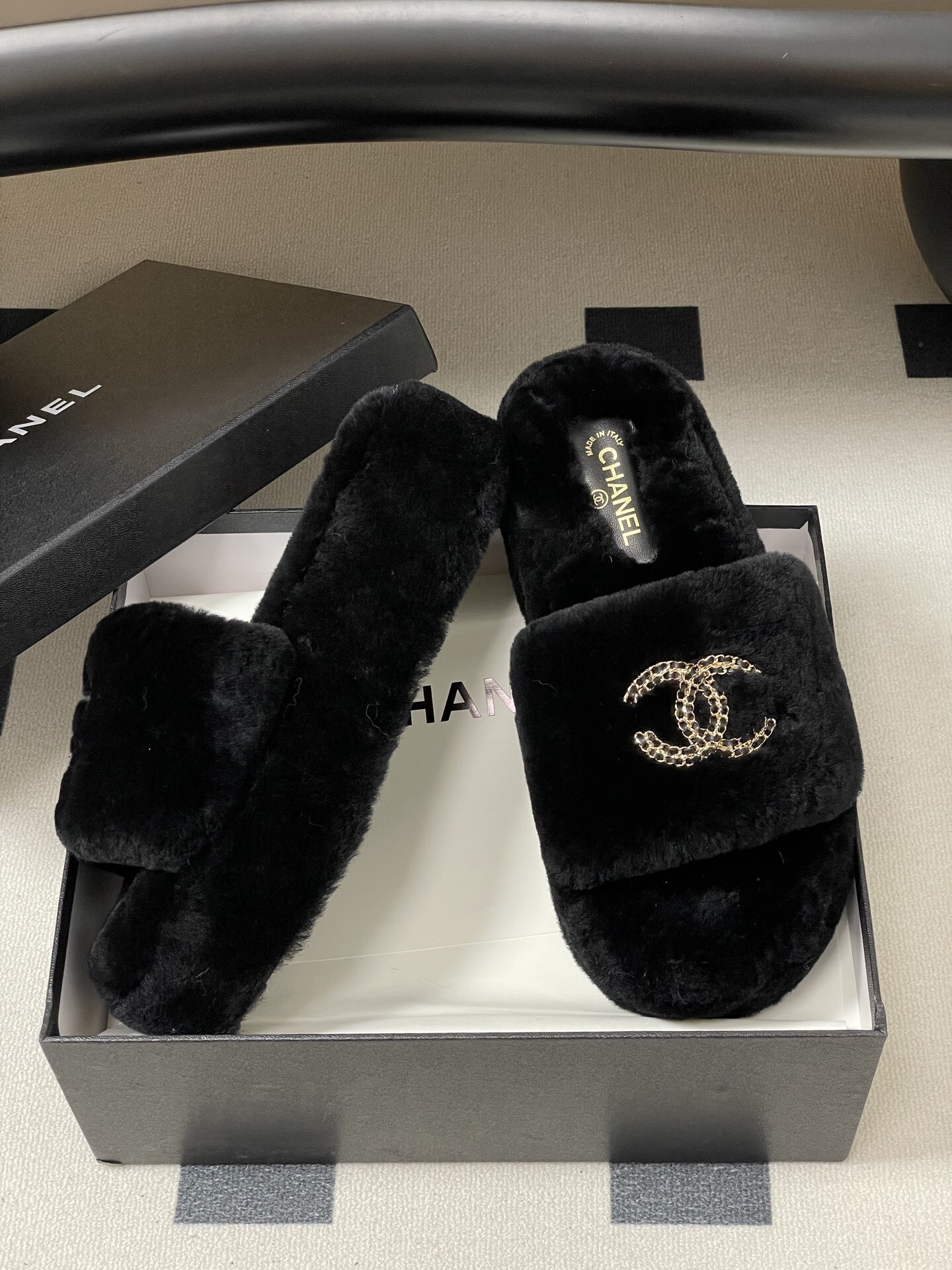 Pair of black Chanel shearling platform slides with gold chain interlocking CC logo on a black table. - Hình 6