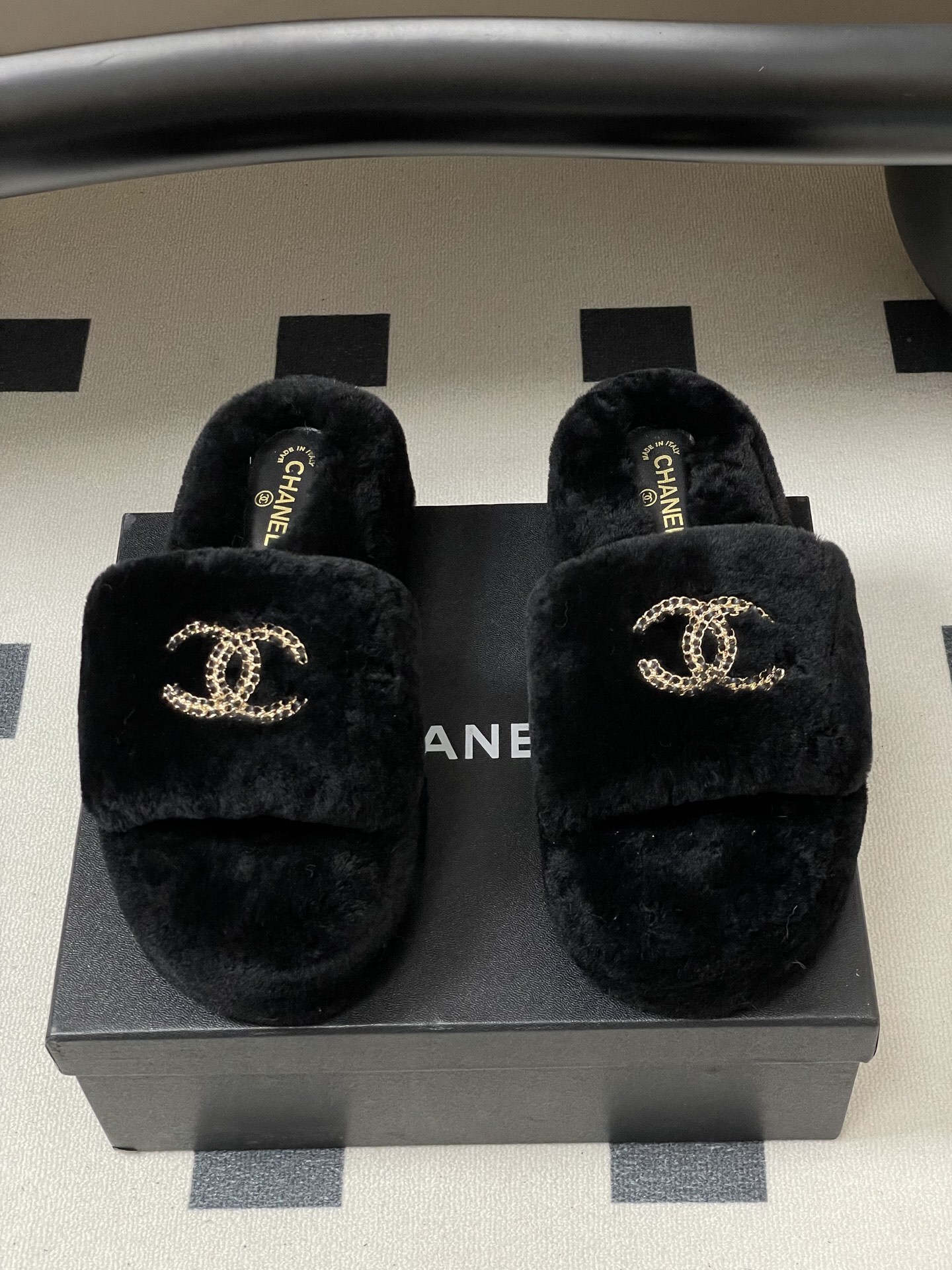 Pair of black Chanel shearling platform slides with gold chain interlocking CC logo on a black table. - Hình 5