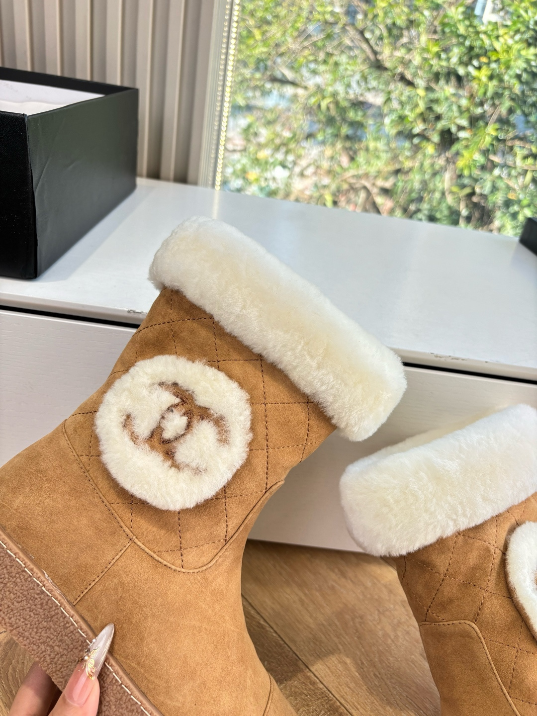 A pair of luxury tan suede winter boots with white shearling trim and a plush logo patch displayed on a white surface. - Hình 8