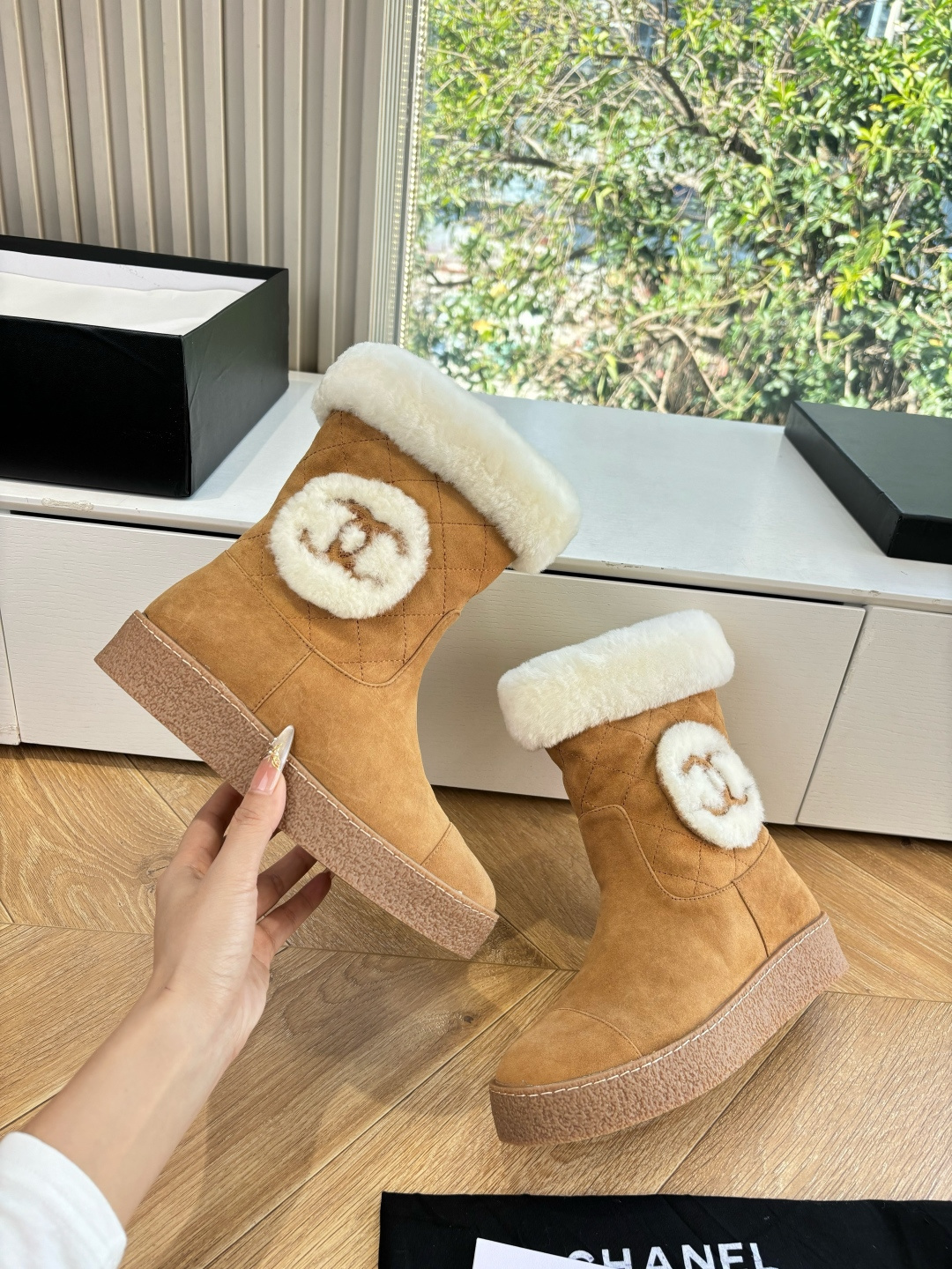 A pair of luxury tan suede winter boots with white shearling trim and a plush logo patch displayed on a white surface. - Hình 7
