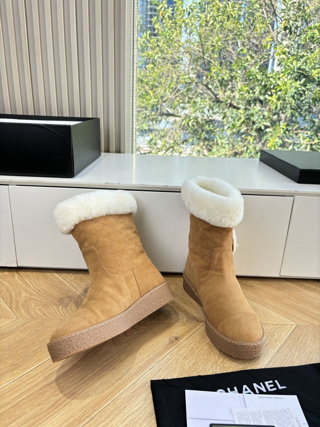 A pair of luxury tan suede winter boots with white shearling trim and a plush logo patch displayed on a white surface. - Hình 6
