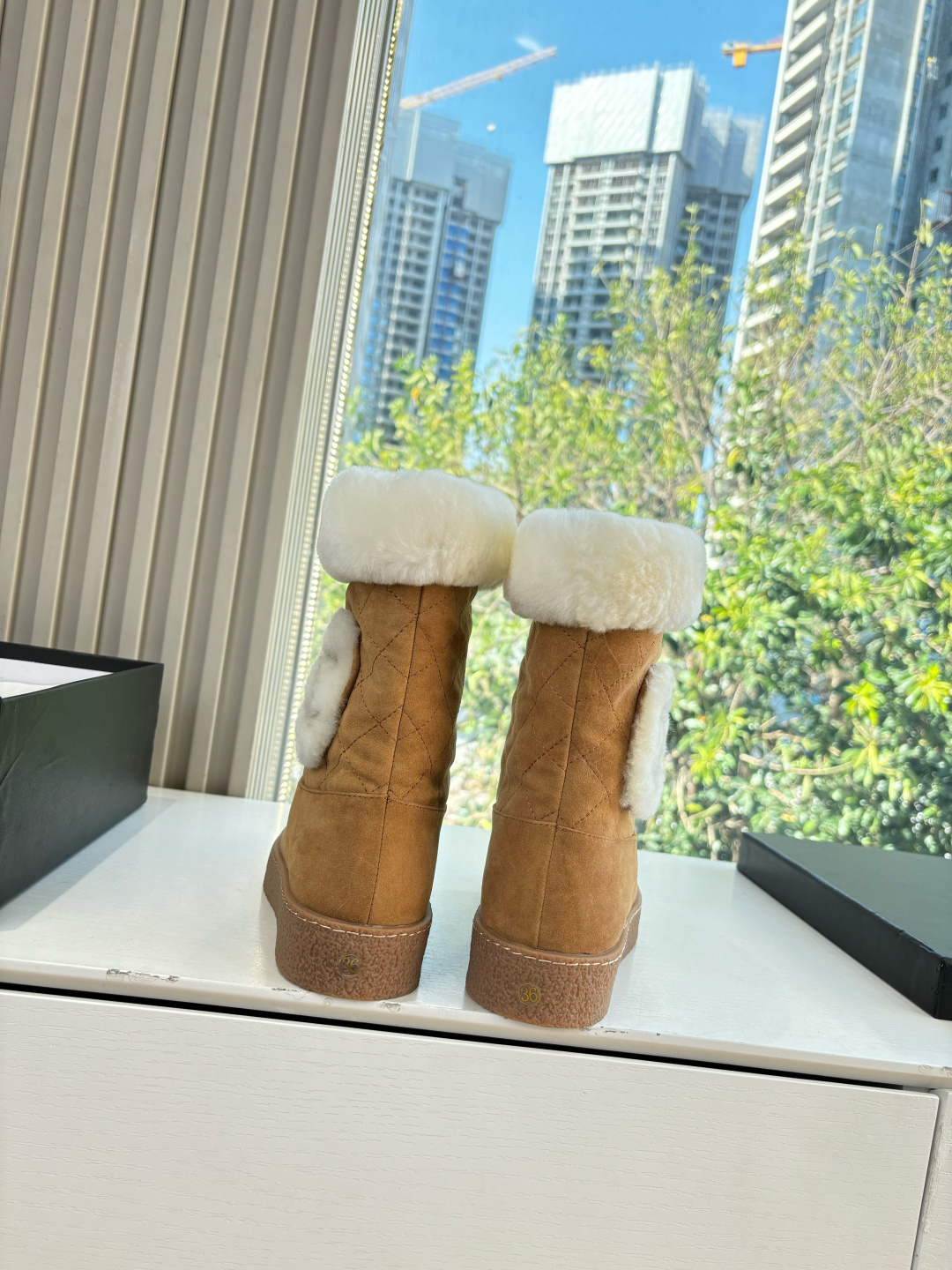 A pair of luxury tan suede winter boots with white shearling trim and a plush logo patch displayed on a white surface. - Hình 4