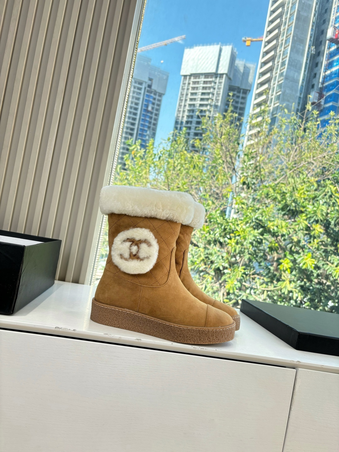 A pair of luxury tan suede winter boots with white shearling trim and a plush logo patch displayed on a white surface. - Hình 3