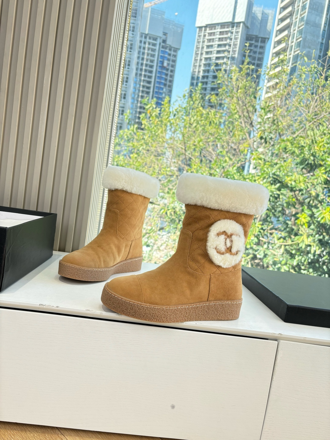 A pair of luxury tan suede winter boots with white shearling trim and a plush logo patch displayed on a white surface. - Hình 2