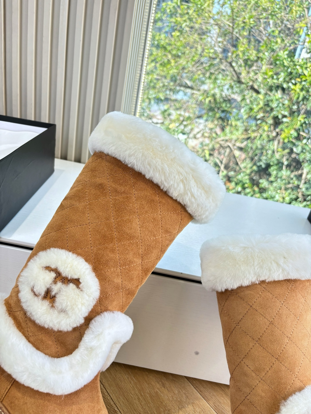 Pair of camel-colored quilted suede tall boots with white faux fur trim and circular logo detail on a white surface - Hình 8