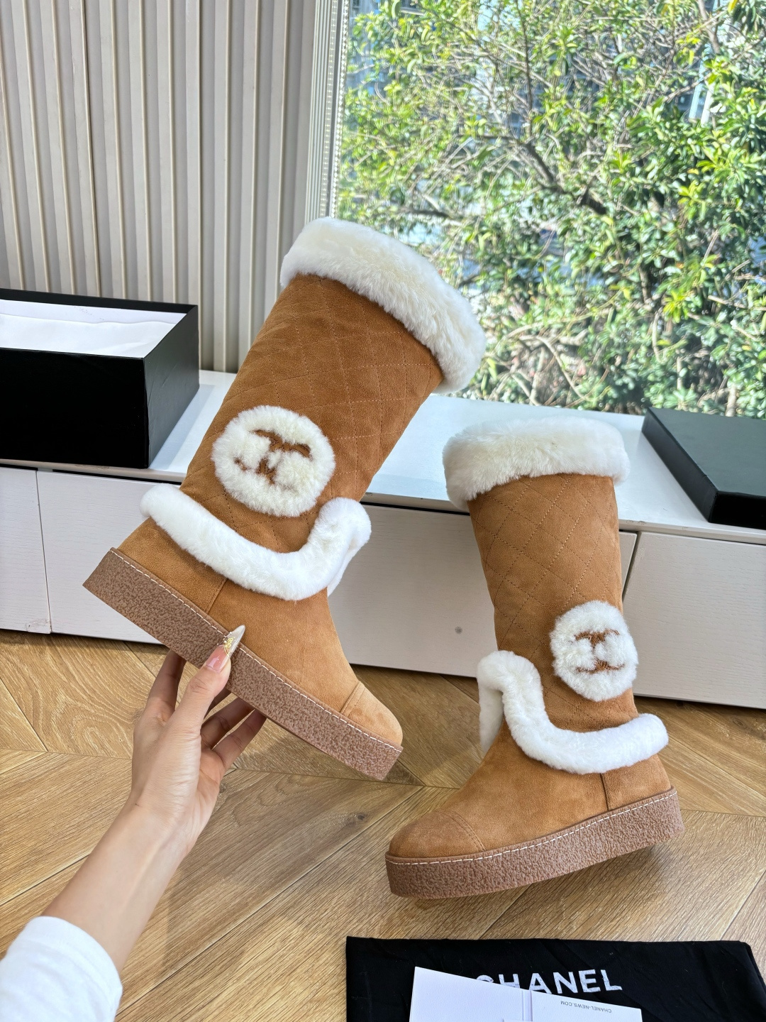 Pair of camel-colored quilted suede tall boots with white faux fur trim and circular logo detail on a white surface - Hình 7