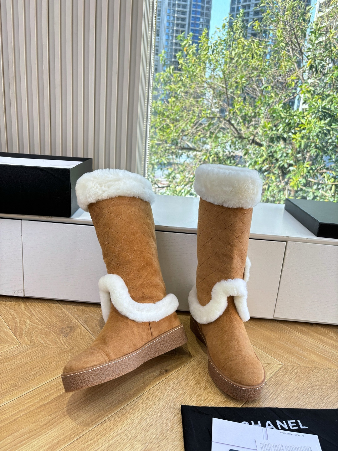 Pair of camel-colored quilted suede tall boots with white faux fur trim and circular logo detail on a white surface - Hình 6