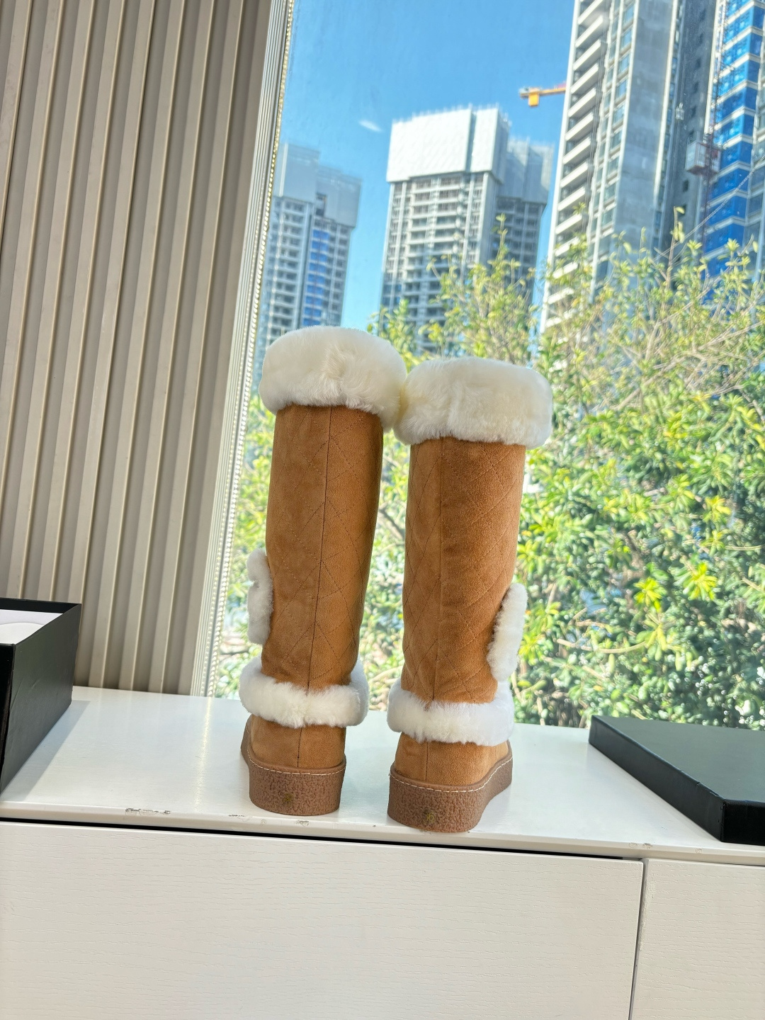 Pair of camel-colored quilted suede tall boots with white faux fur trim and circular logo detail on a white surface - Hình 4