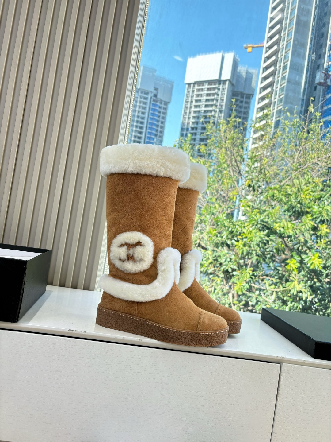 Pair of camel-colored quilted suede tall boots with white faux fur trim and circular logo detail on a white surface - Hình 3