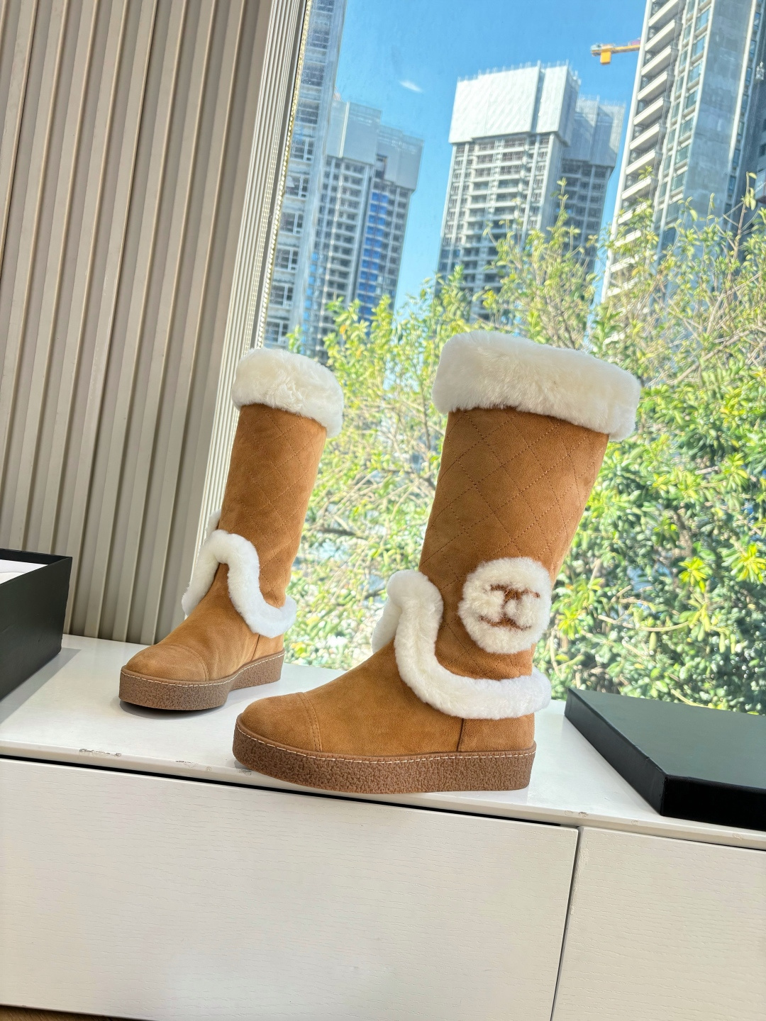 Pair of camel-colored quilted suede tall boots with white faux fur trim and circular logo detail on a white surface - Hình 2