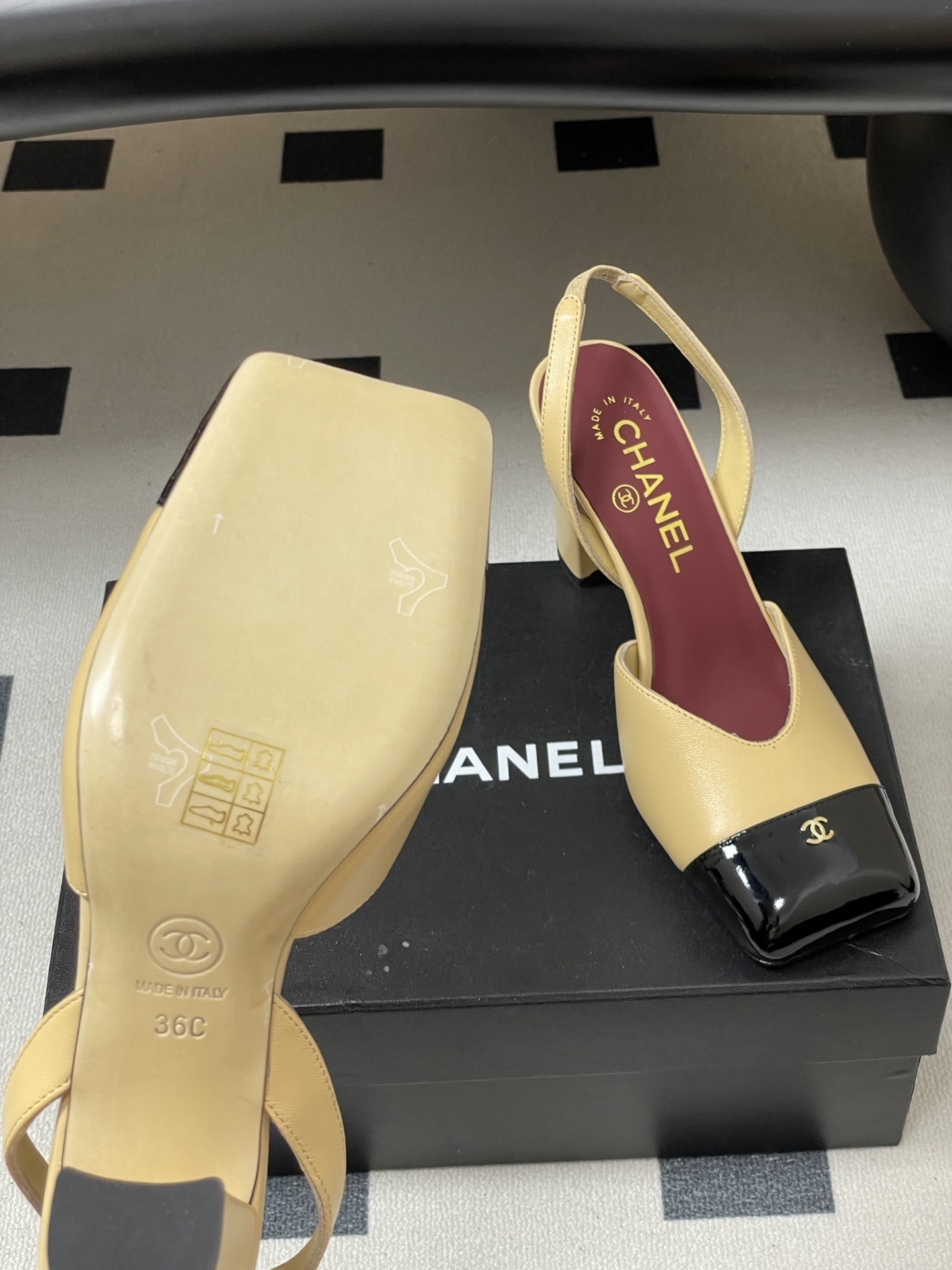 A pair of Chanel two-tone beige and black square toe slingback heels with block heels and gold CC logo on a black surface. - Hình 8