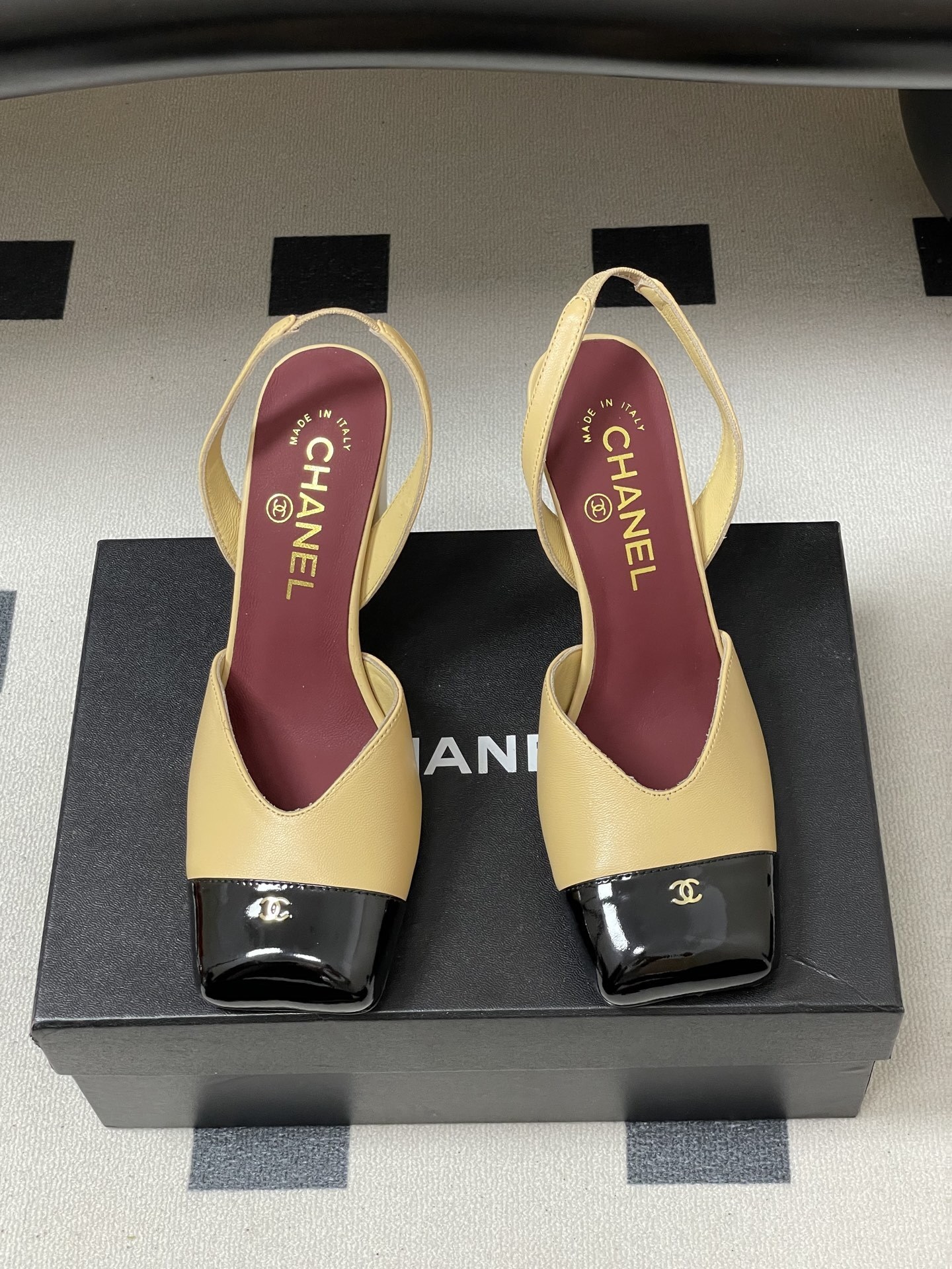 A pair of Chanel two-tone beige and black square toe slingback heels with block heels and gold CC logo on a black surface. - Hình 5