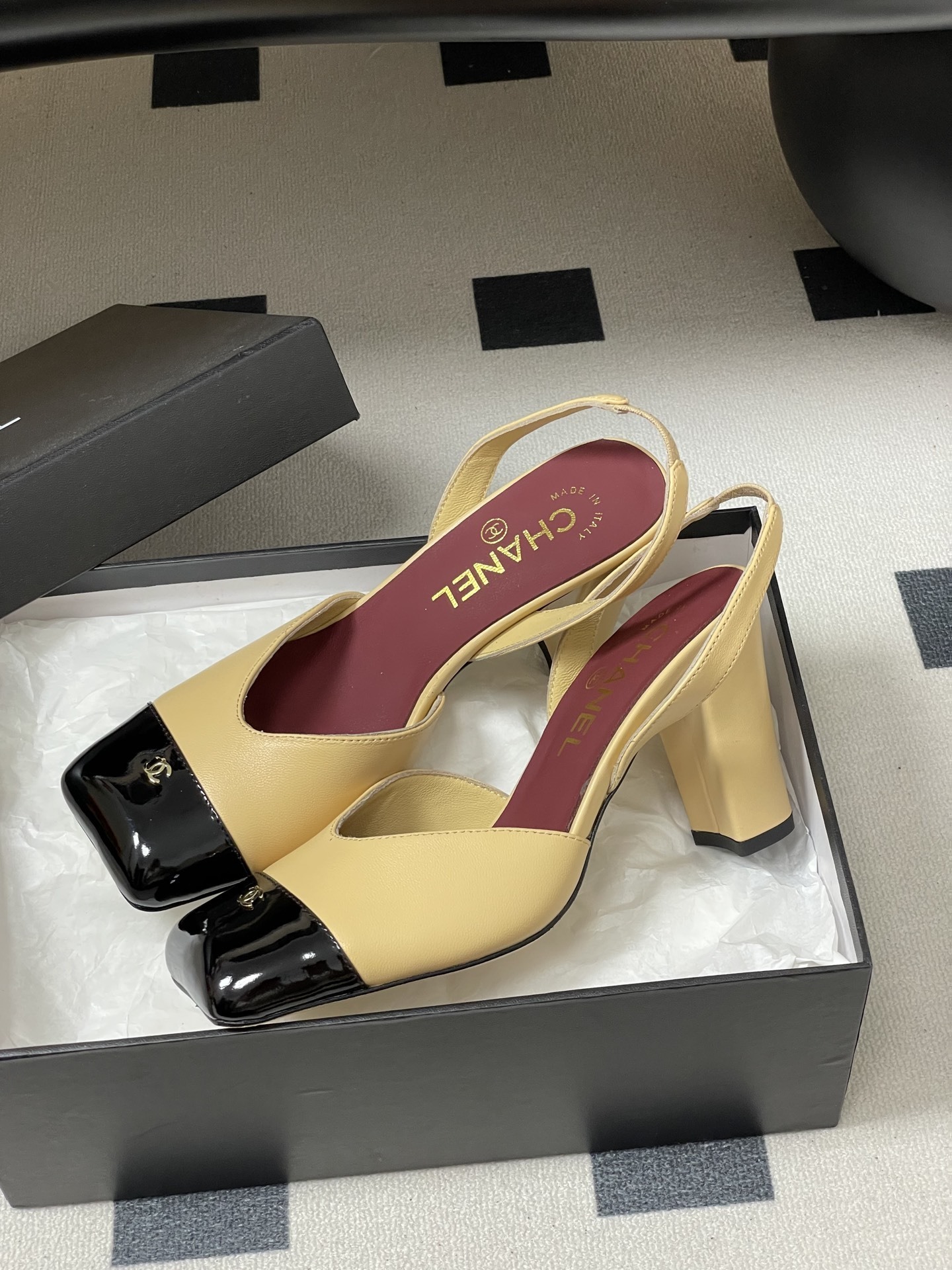 A pair of Chanel two-tone beige and black square toe slingback heels with block heels and gold CC logo on a black surface. - Hình 4