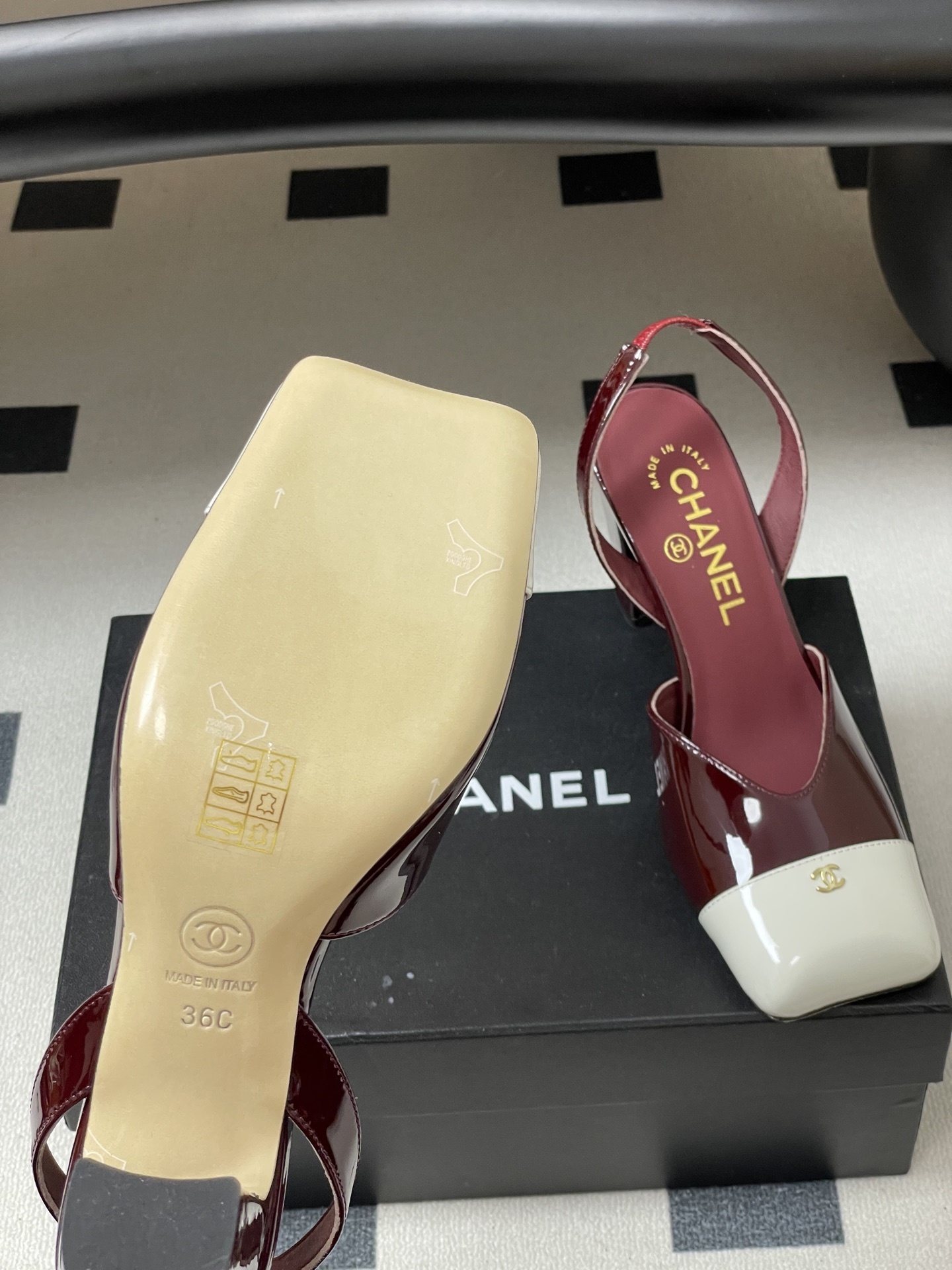 A pair of Chanel burgundy patent leather slingback pumps with a white square toe cap and gold CC logo on a black table. - Hình 8