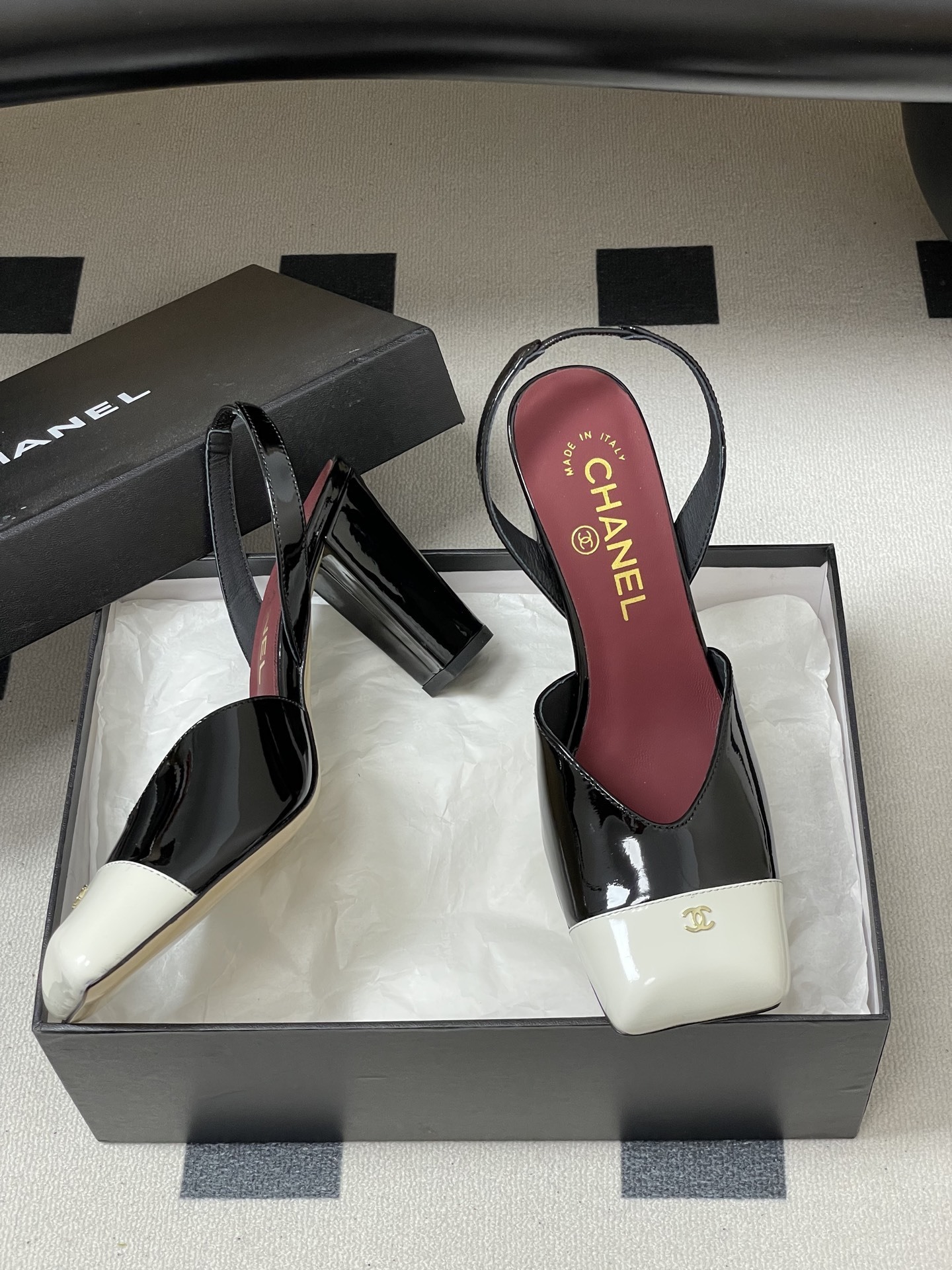 Pair of Chanel black patent leather slingback heels with white square toe caps and gold CC logo on a black table. - Hình 6