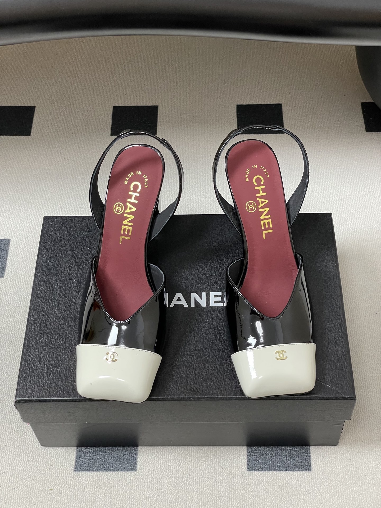 Pair of Chanel black patent leather slingback heels with white square toe caps and gold CC logo on a black table. - Hình 5