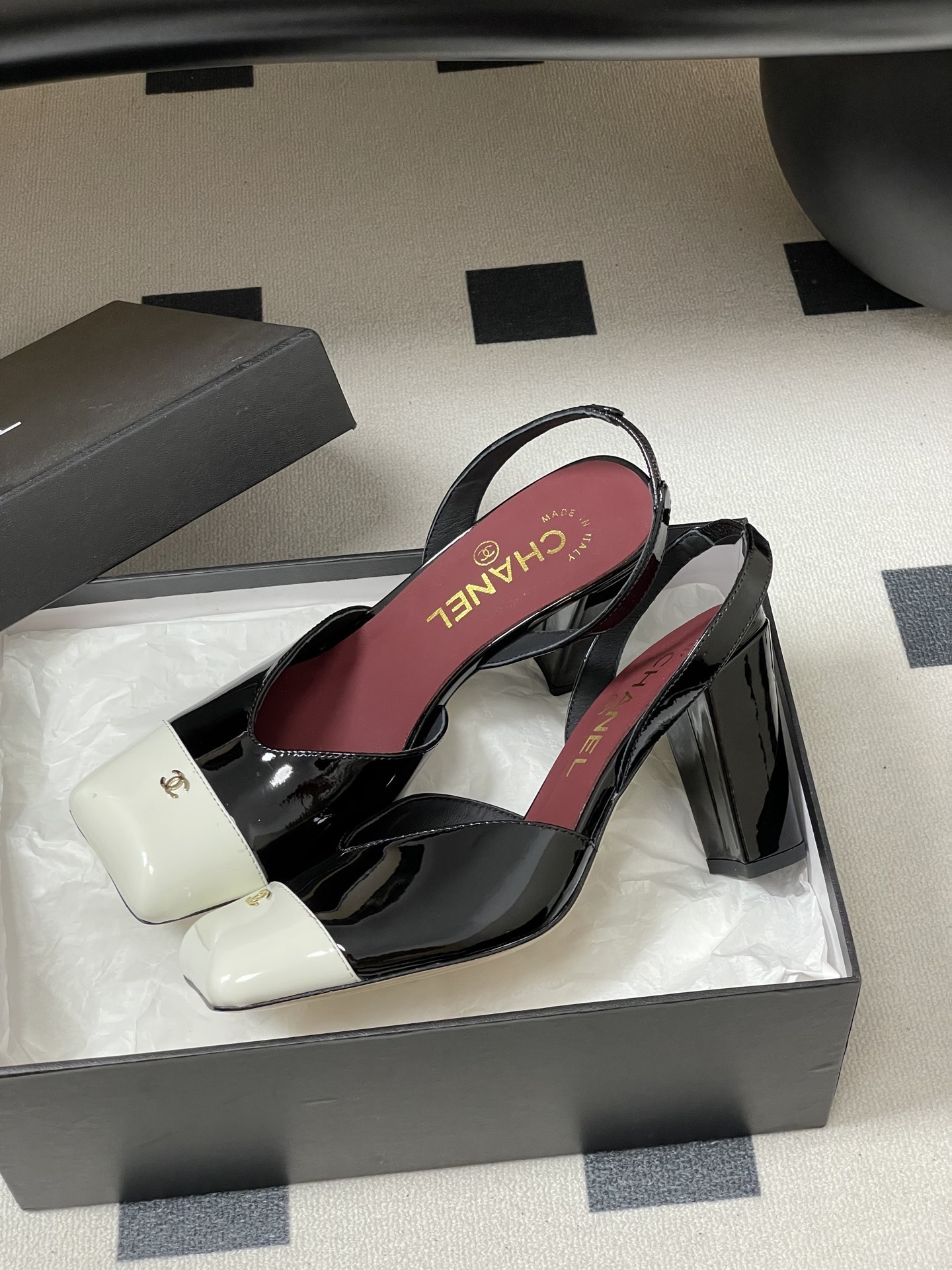 Pair of Chanel black patent leather slingback heels with white square toe caps and gold CC logo on a black table. - Hình 4