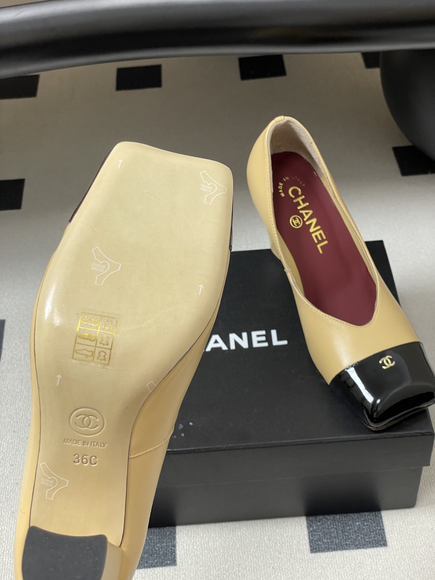 A pair of Chanel beige leather pumps featuring a black patent leather square toe cap with gold CC logo and a sturdy block heel. - Hình 8