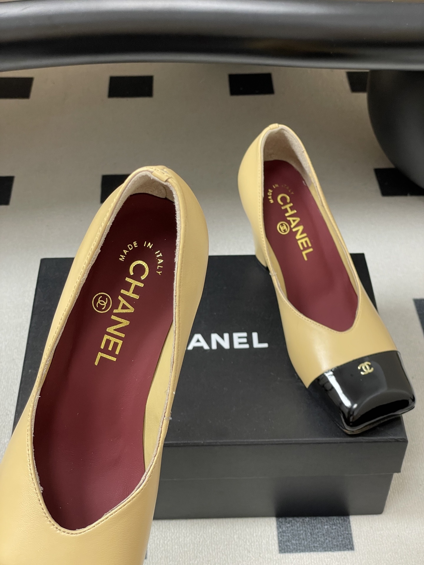 A pair of Chanel beige leather pumps featuring a black patent leather square toe cap with gold CC logo and a sturdy block heel. - Hình 7
