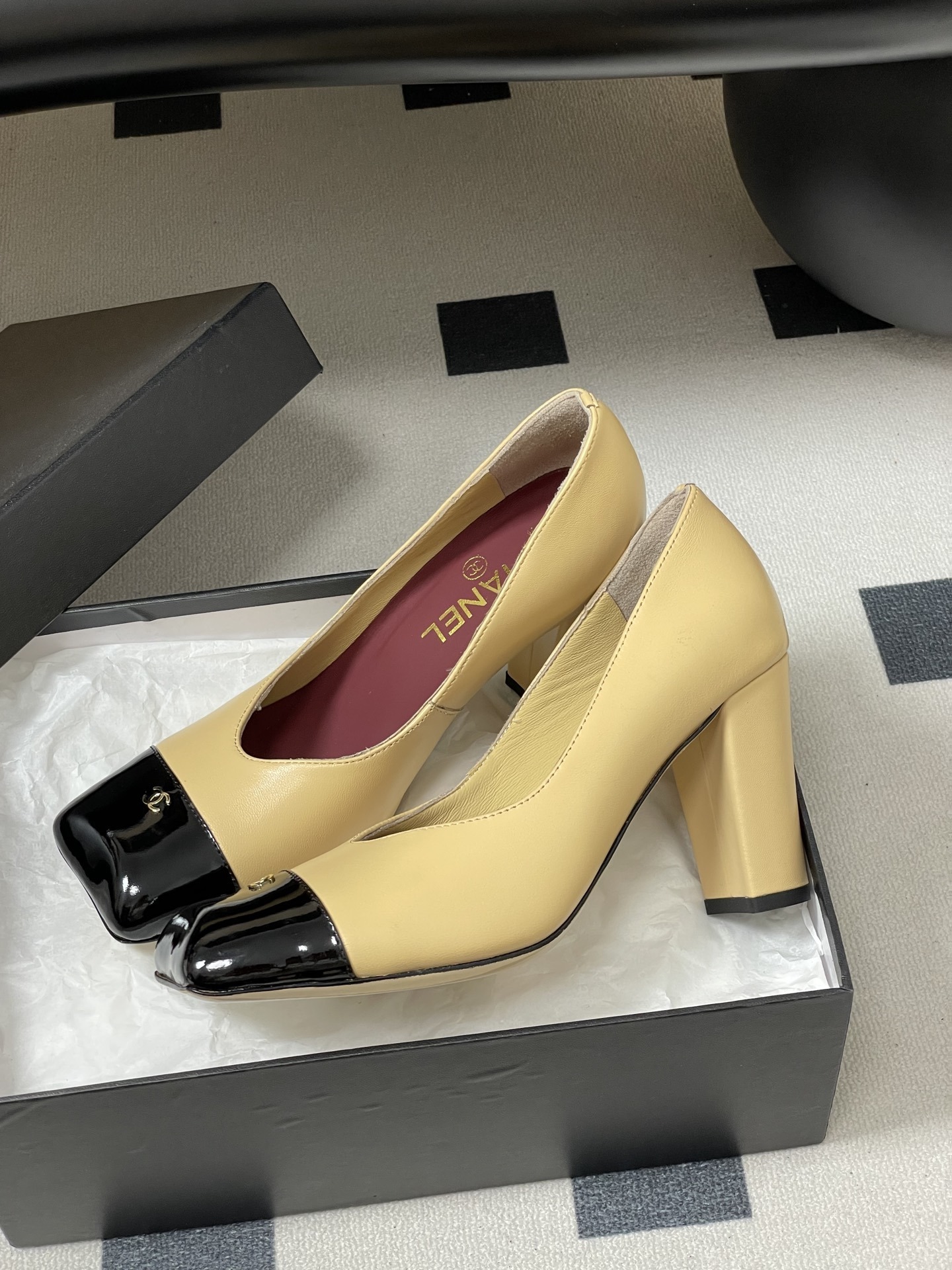 A pair of Chanel beige leather pumps featuring a black patent leather square toe cap with gold CC logo and a sturdy block heel. - Hình 4