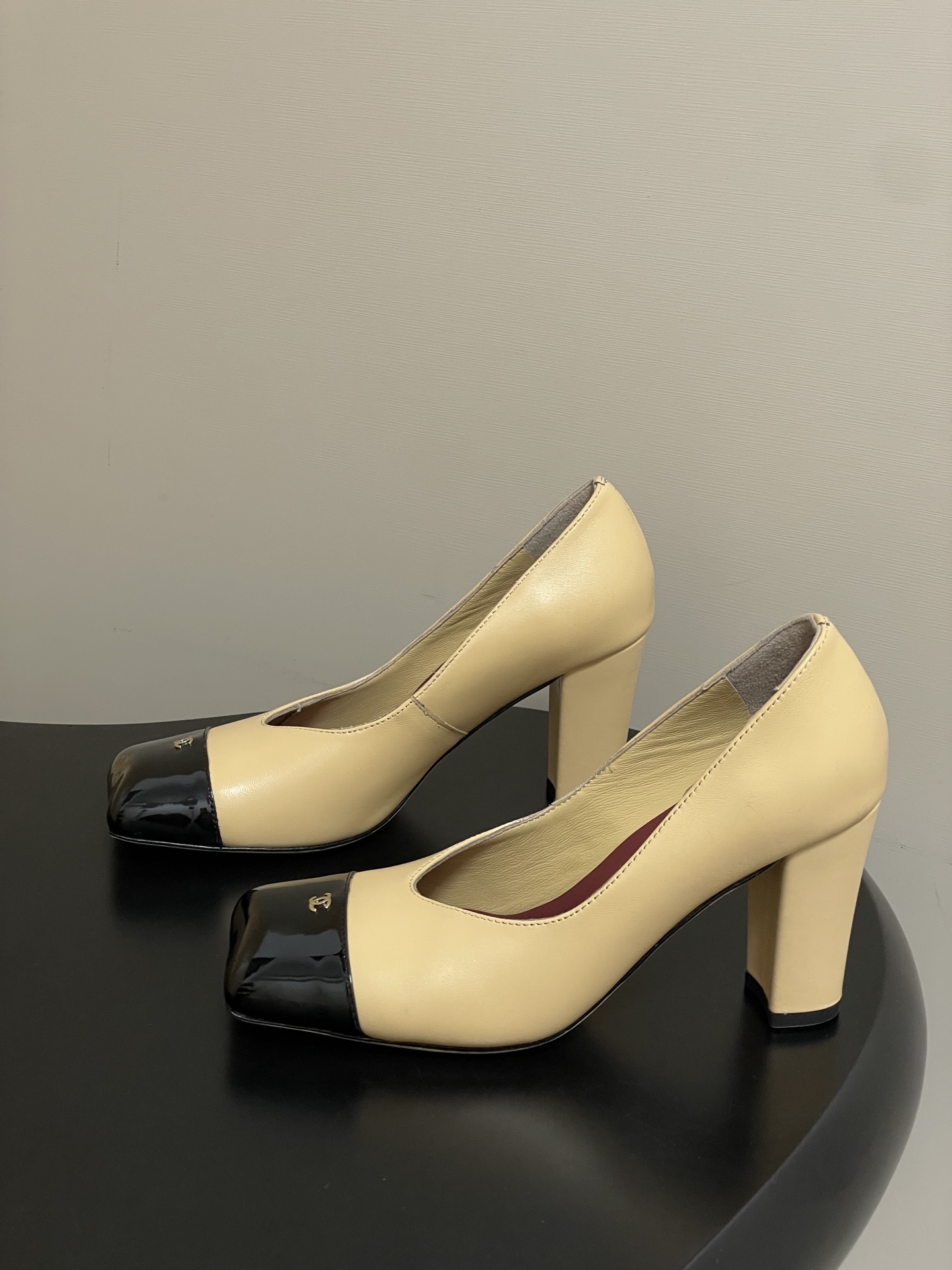 A pair of Chanel beige leather pumps featuring a black patent leather square toe cap with gold CC logo and a sturdy block heel. - Hình 3