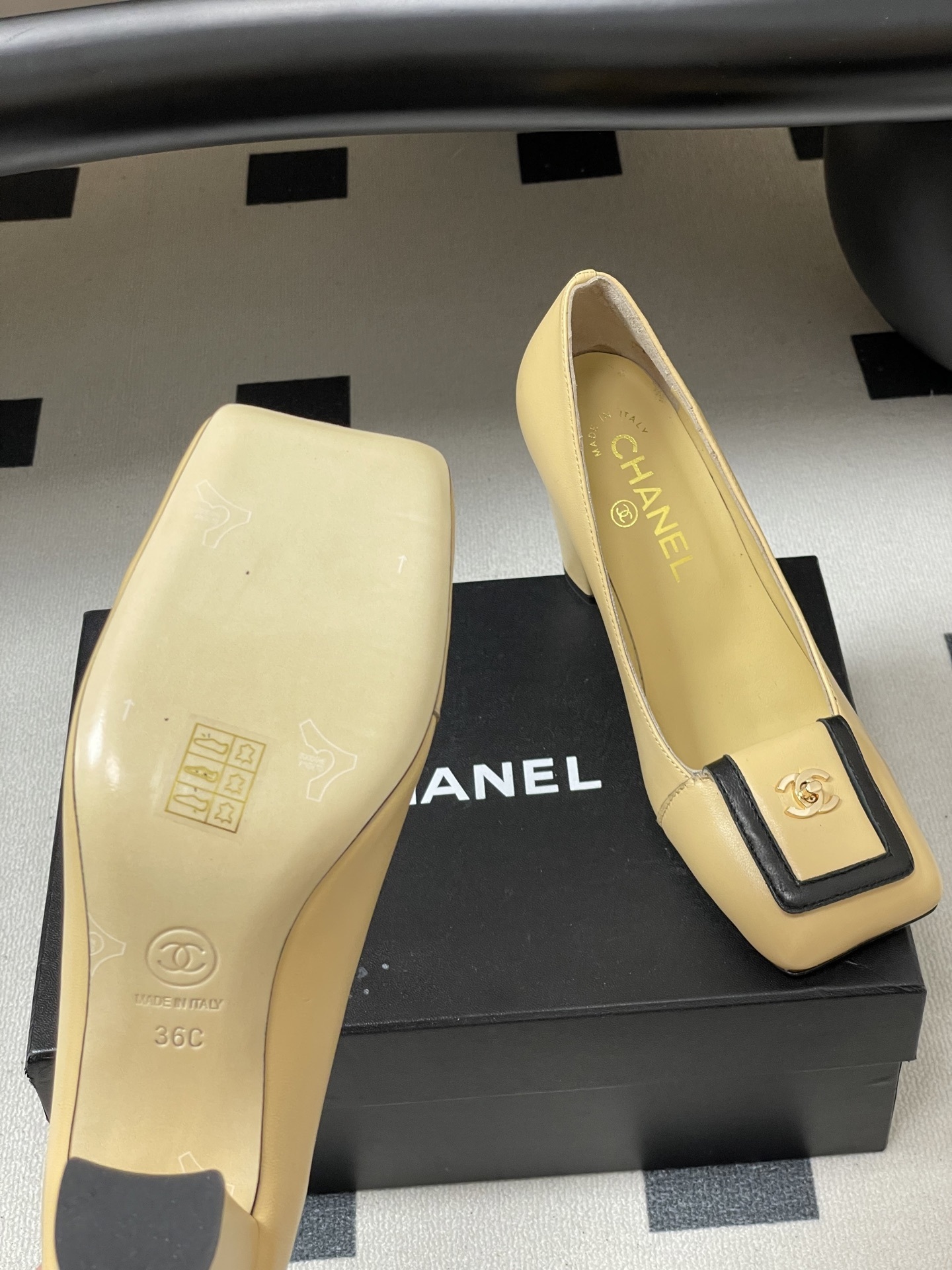 A pair of luxury Chanel beige leather block heel pumps with black trim and gold CC logo detailing on a black surface. - Hình 8