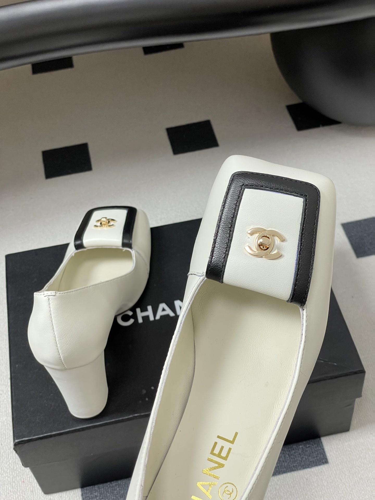 Pair of Chanel white leather square toe pumps with black trim and gold CC logo on a black surface. - Hình 9