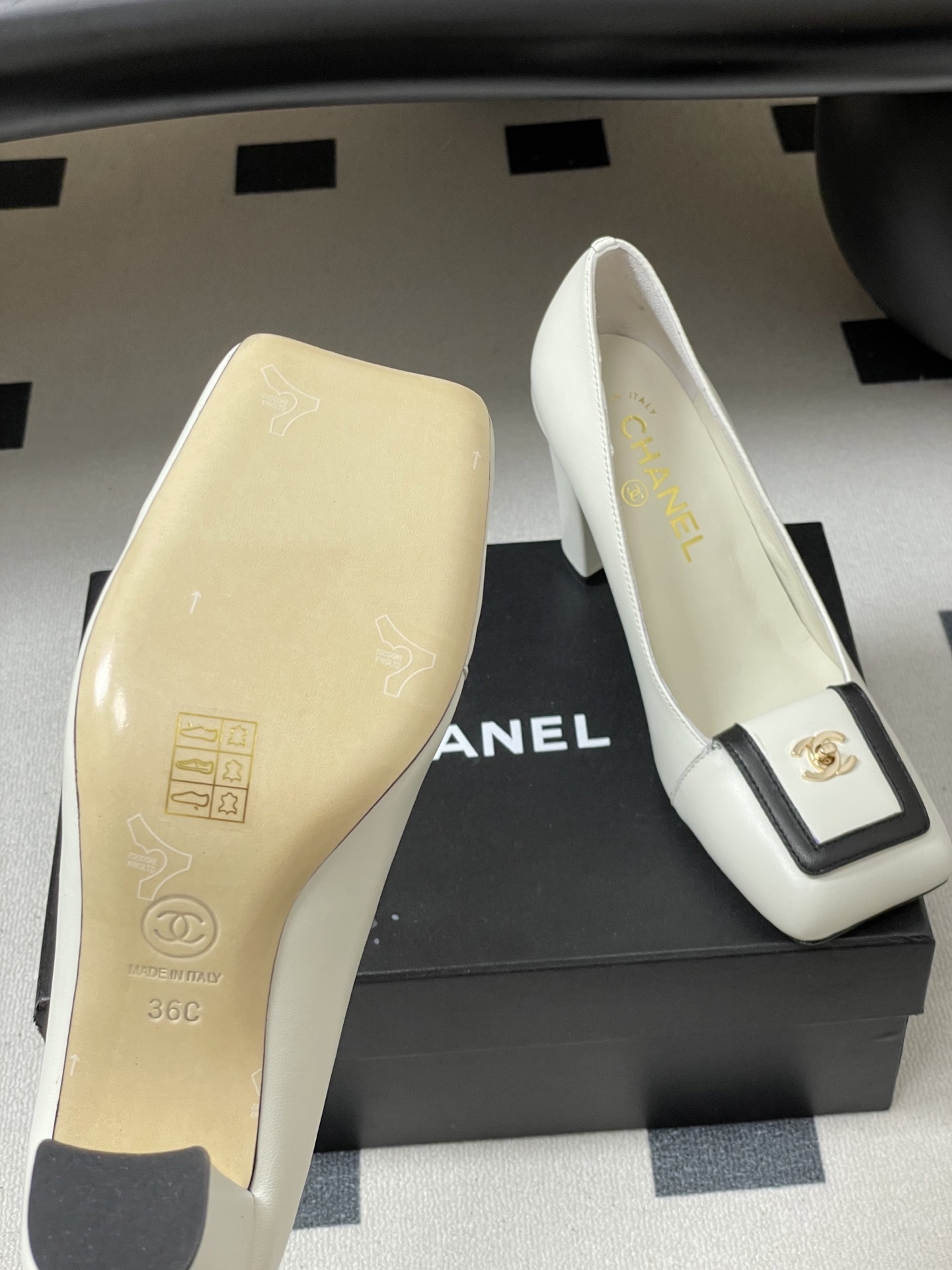 Pair of Chanel white leather square toe pumps with black trim and gold CC logo on a black surface. - Hình 8