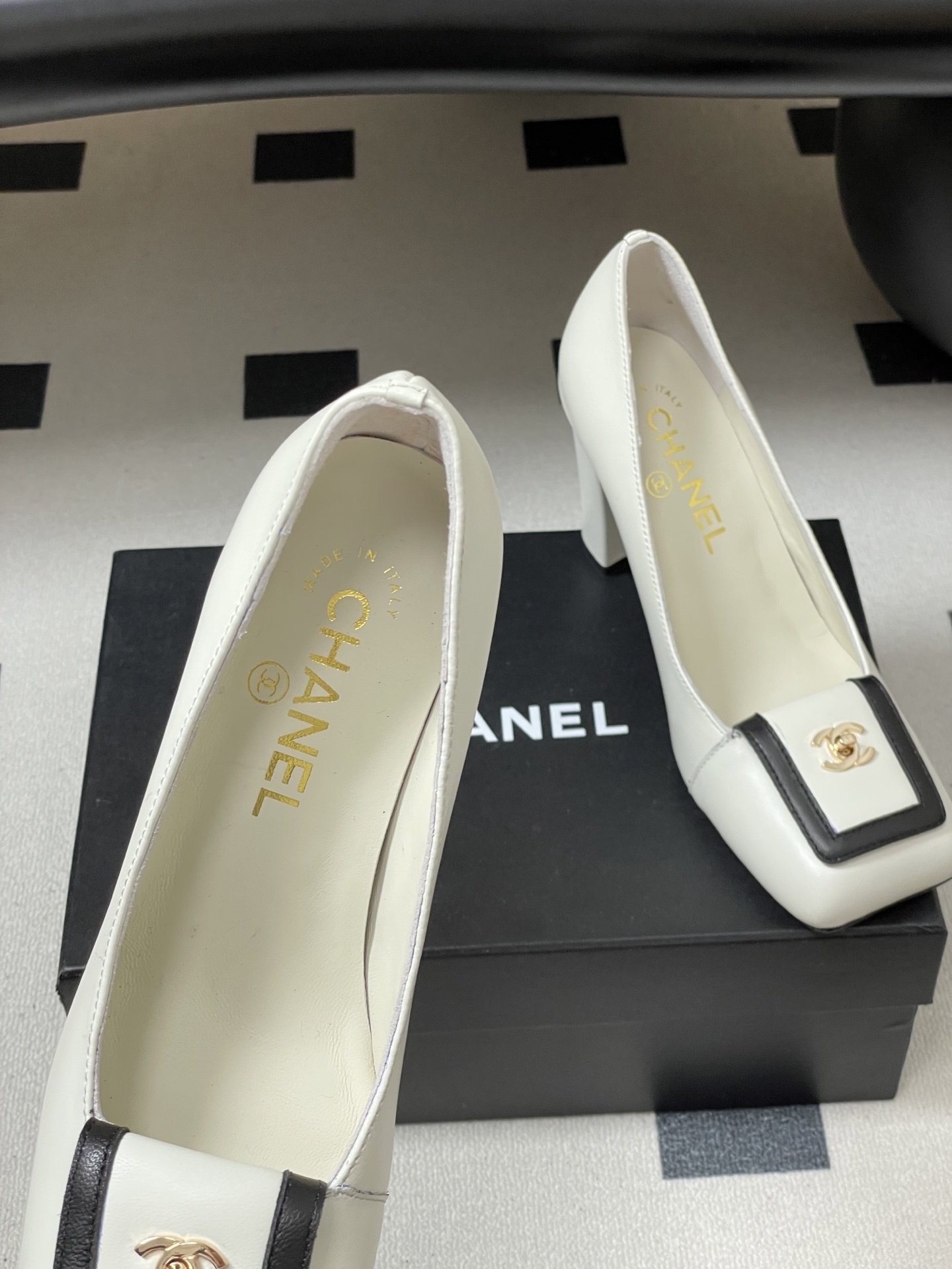 Pair of Chanel white leather square toe pumps with black trim and gold CC logo on a black surface. - Hình 7