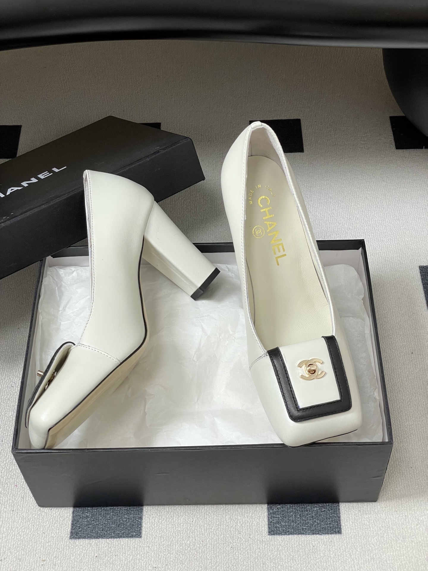 Pair of Chanel white leather square toe pumps with black trim and gold CC logo on a black surface. - Hình 6
