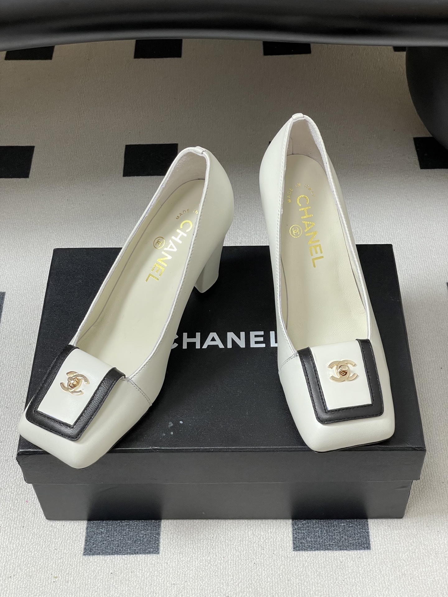 Pair of Chanel white leather square toe pumps with black trim and gold CC logo on a black surface. - Hình 5