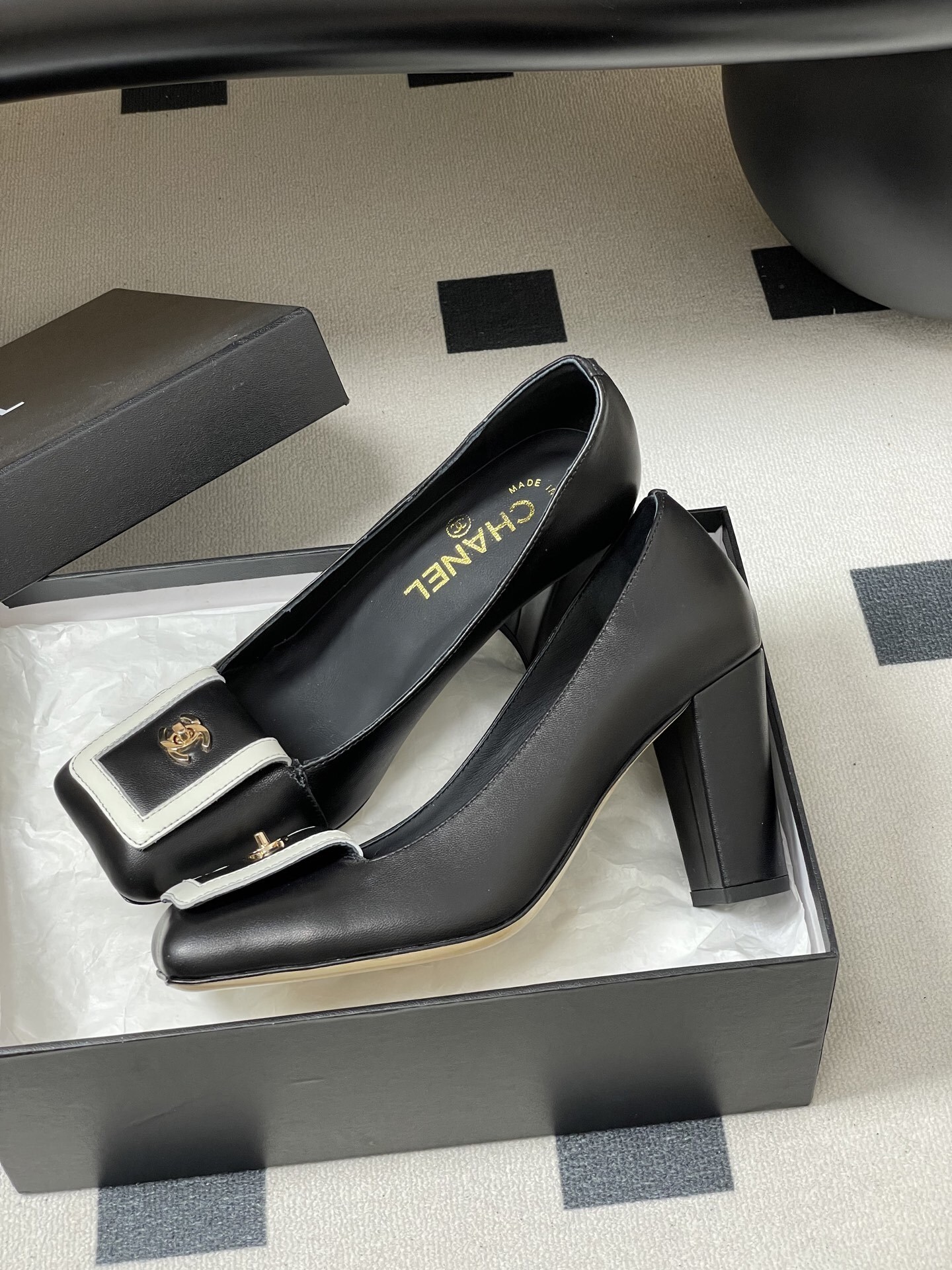 A pair of Chanel black leather block heel pumps with square toes and gold-tone CC logos on white buckle details. - Hình 4