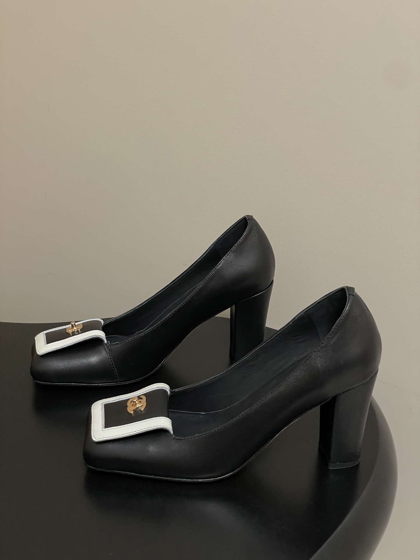 A pair of Chanel black leather block heel pumps with square toes and gold-tone CC logos on white buckle details. - Hình 3