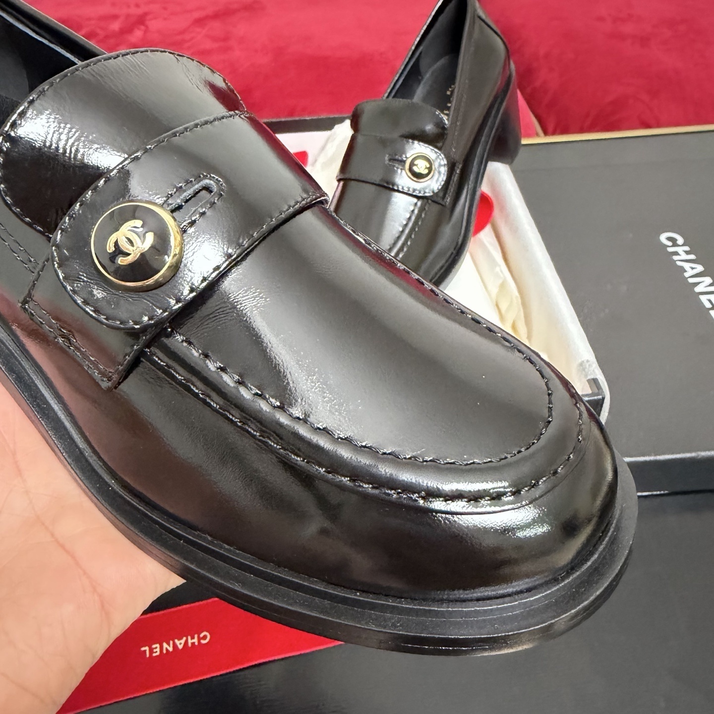 Luxury black Chanel patent leather loafers with gold CC logo buttons displayed in a box with red ribbons - Hình 6