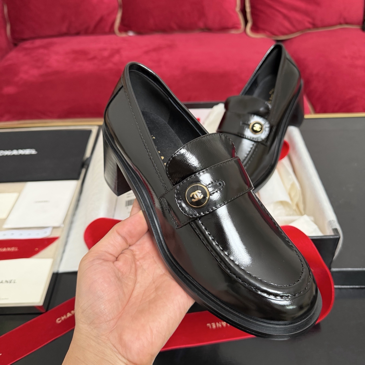 Luxury black Chanel patent leather loafers with gold CC logo buttons displayed in a box with red ribbons - Hình 4