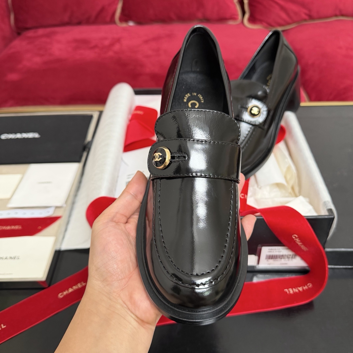 Luxury black Chanel patent leather loafers with gold CC logo buttons displayed in a box with red ribbons - Hình 3