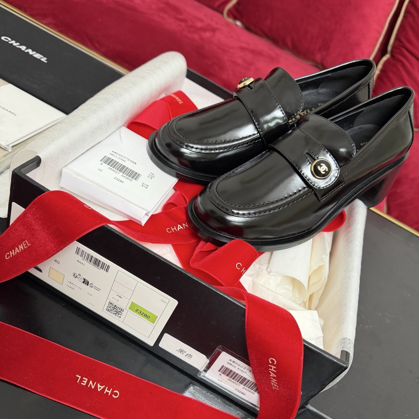 Luxury black Chanel patent leather loafers with gold CC logo buttons displayed in a box with red ribbons - Hình 2