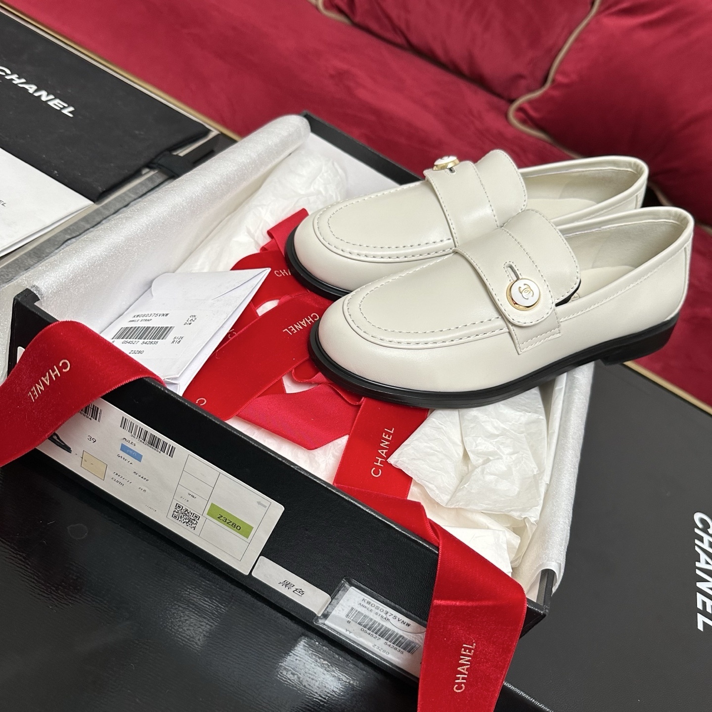 Pair of ivory Chanel leather loafers with gold CC logo buttons in original packaging with red ribbons. - Hình 2