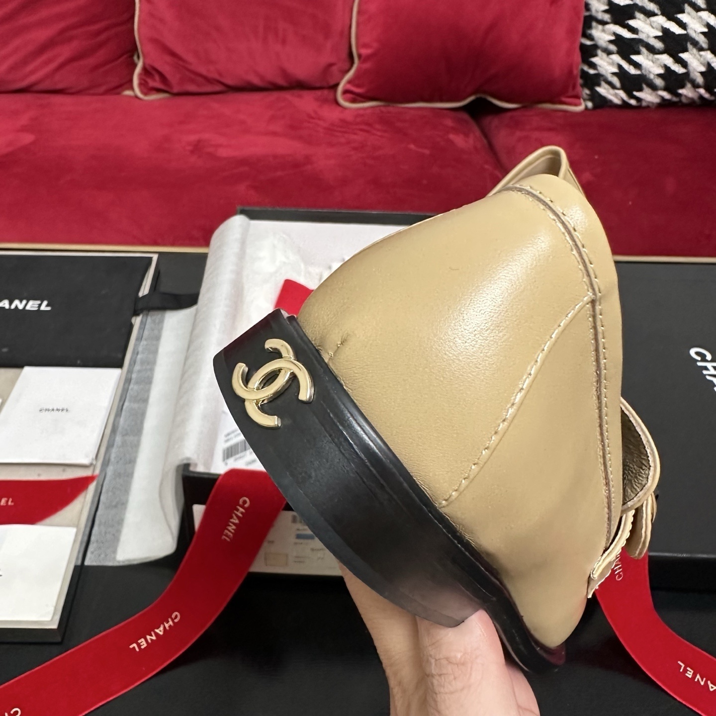 A pair of Chanel beige leather loafers with gold CC logo buttons presented in a luxury black box with red ribbons. - Hình 8