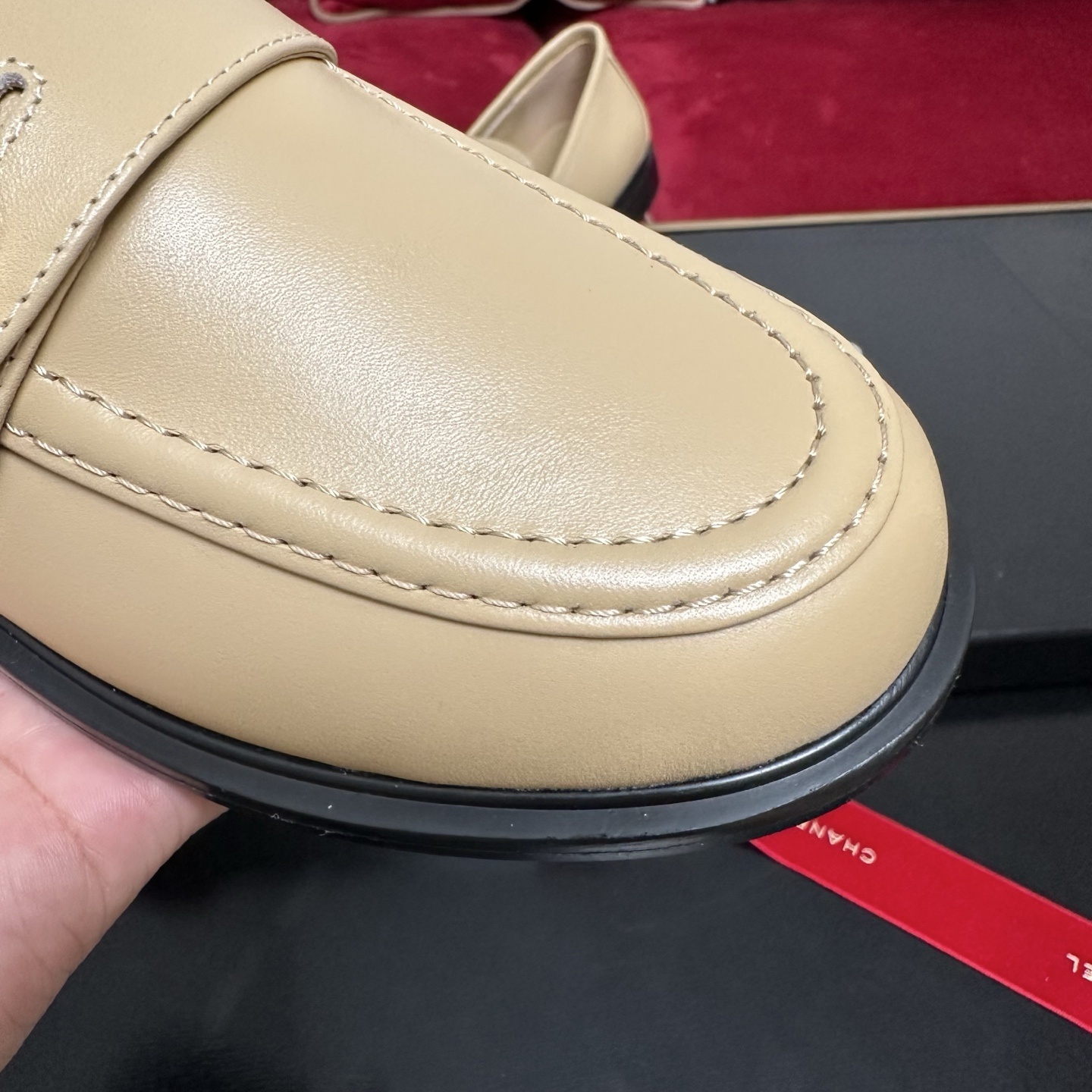 A pair of Chanel beige leather loafers with gold CC logo buttons presented in a luxury black box with red ribbons. - Hình 6