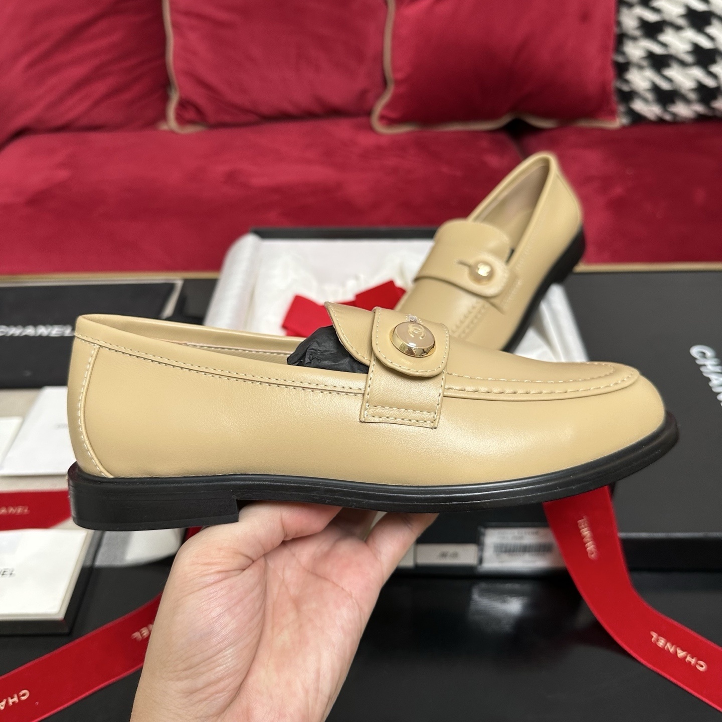 A pair of Chanel beige leather loafers with gold CC logo buttons presented in a luxury black box with red ribbons. - Hình 5