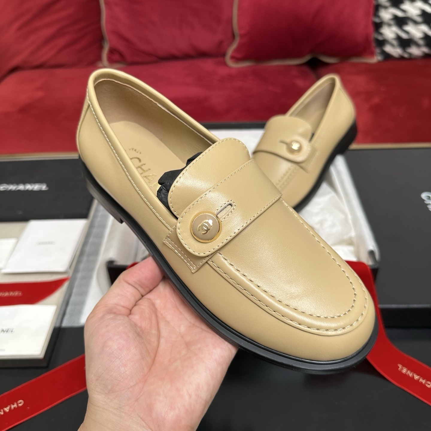 A pair of Chanel beige leather loafers with gold CC logo buttons presented in a luxury black box with red ribbons. - Hình 4