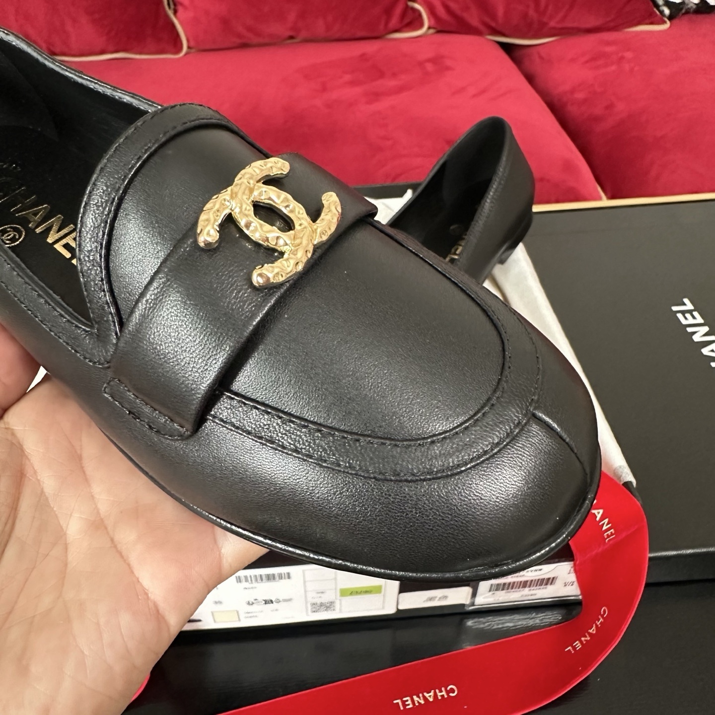 Pair of black Chanel leather loafers with gold CC logo on a decorative background with red ribbons and original box. - Hình 6