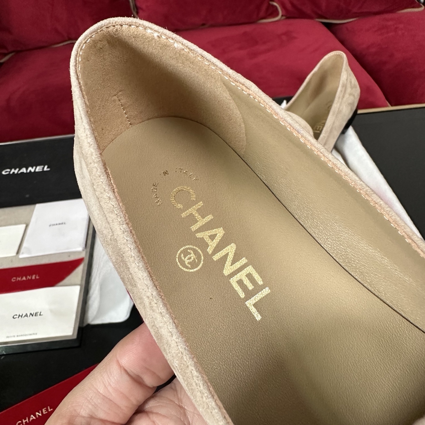Pair of beige Chanel suede loafers with gold and crystal interlocking CC logos on a black surface with red ribbons. - Hình 7