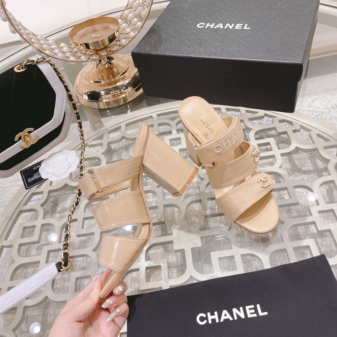 A pair of beige Chanel triple strap block heel mules with gold CC logos and embroidered branding displayed on a glass table. - Hình 8