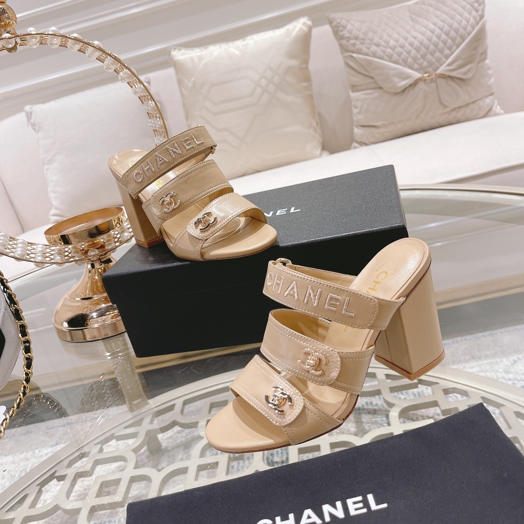 A pair of beige Chanel triple strap block heel mules with gold CC logos and embroidered branding displayed on a glass table. - Hình 5