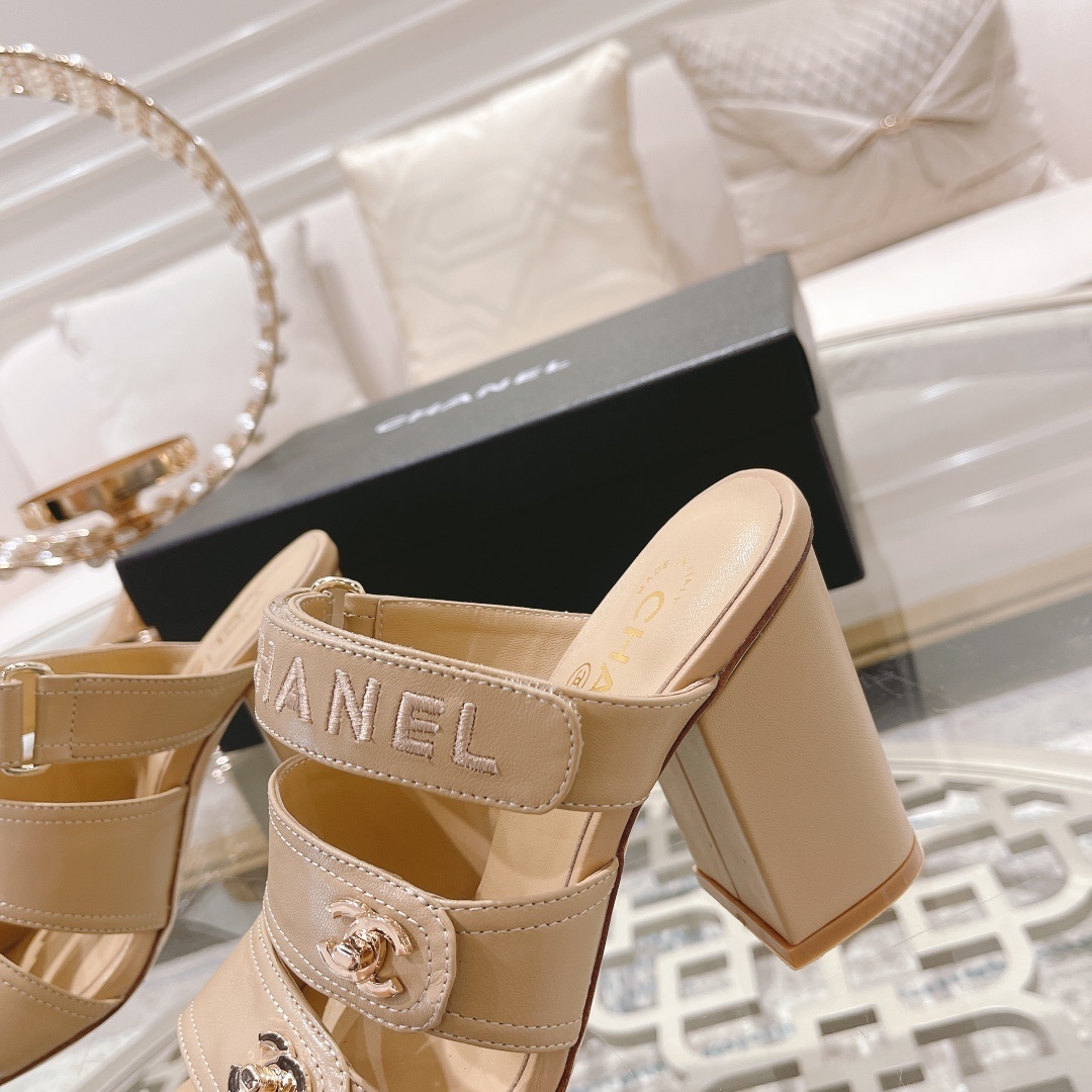 A pair of beige Chanel triple strap block heel mules with gold CC logos and embroidered branding displayed on a glass table. - Hình 4