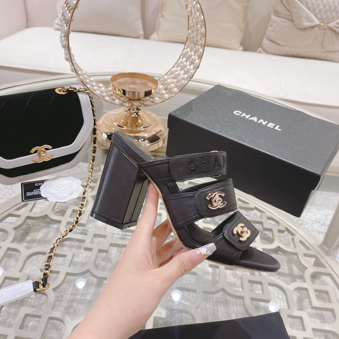 A pair of luxury Chanel black leather triple strap block heel mules with gold CC logos displayed on a glass table - Hình 5