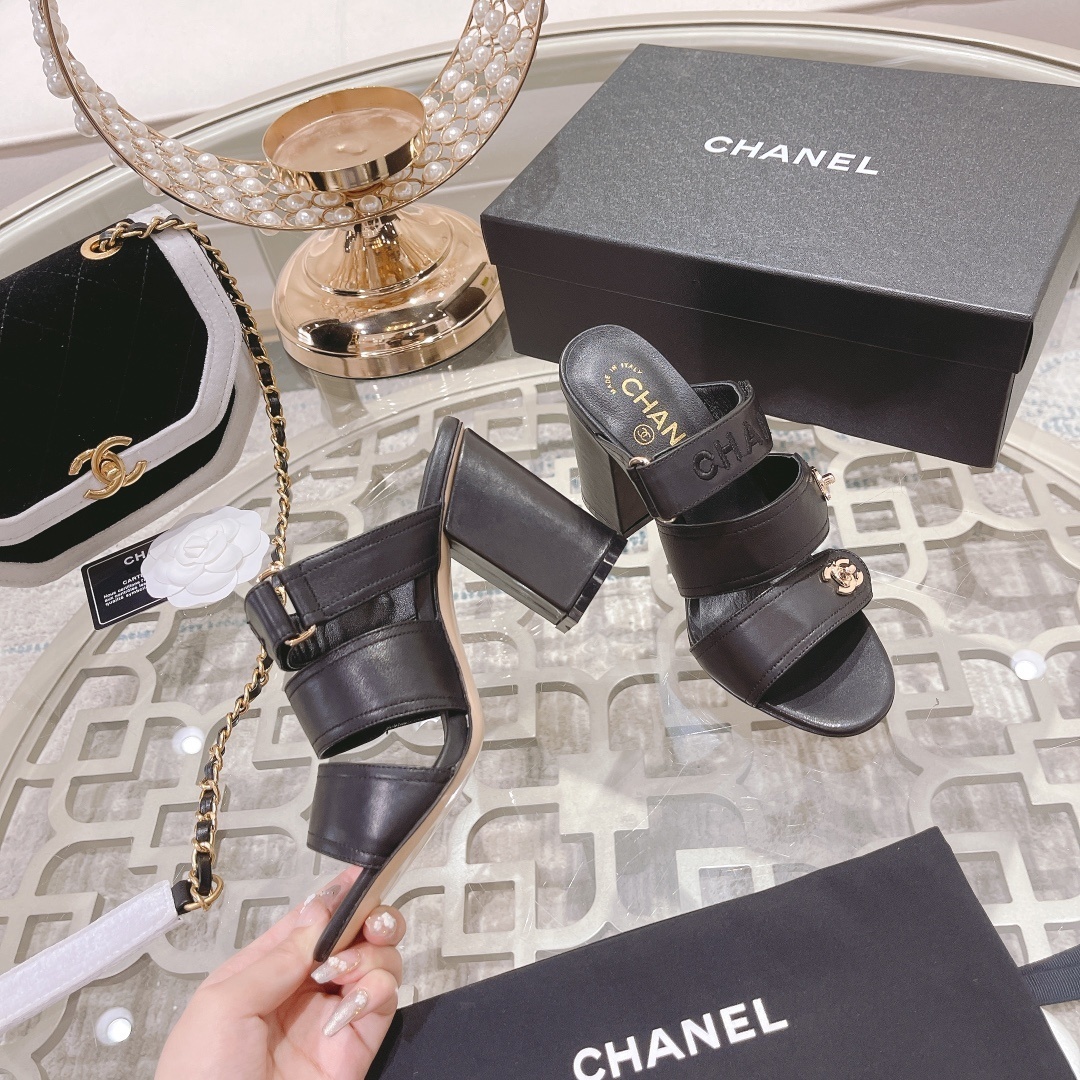 A pair of luxury Chanel black leather triple strap block heel mules with gold CC logos displayed on a glass table - Hình 4